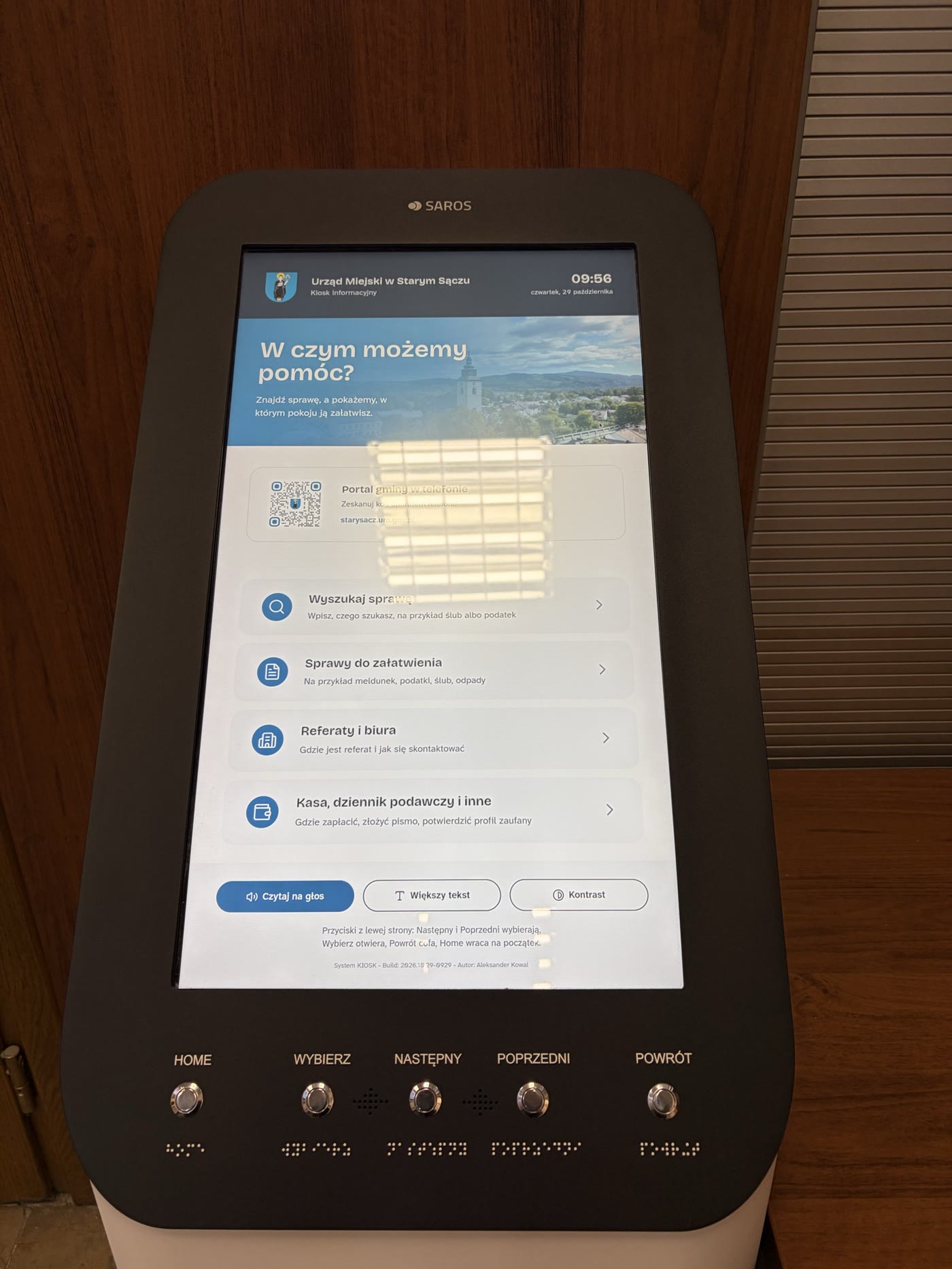 Kiosk w holu urzędu z bliska: ekran startowy, pod nim pięć przycisków z napisami i opisem w alfabecie Braille’a