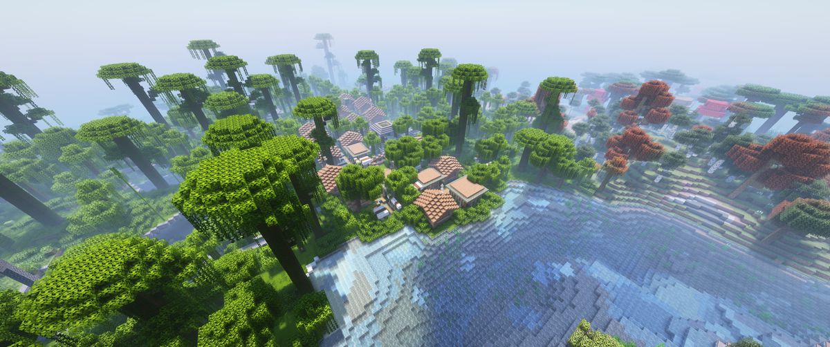Aerial view of a village with red roofs nestled by a river, surrounded by dense forest with green and russet canopies