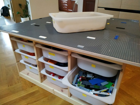 A LEGO table with containers in the shelves and a bowl of bricks on the surface